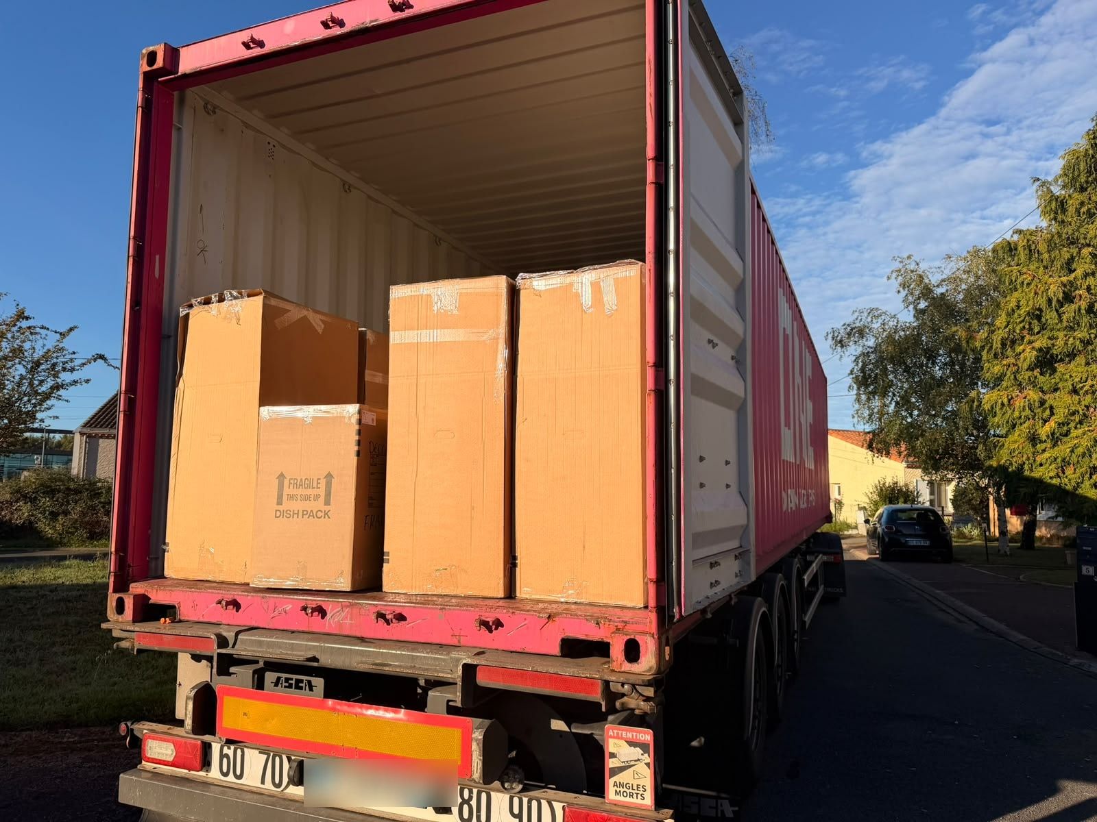 Arrière d’un conteneur maritime ouvert sur une remorque, avec de grands cartons de déménagement identifiés prêts à être déchargés.