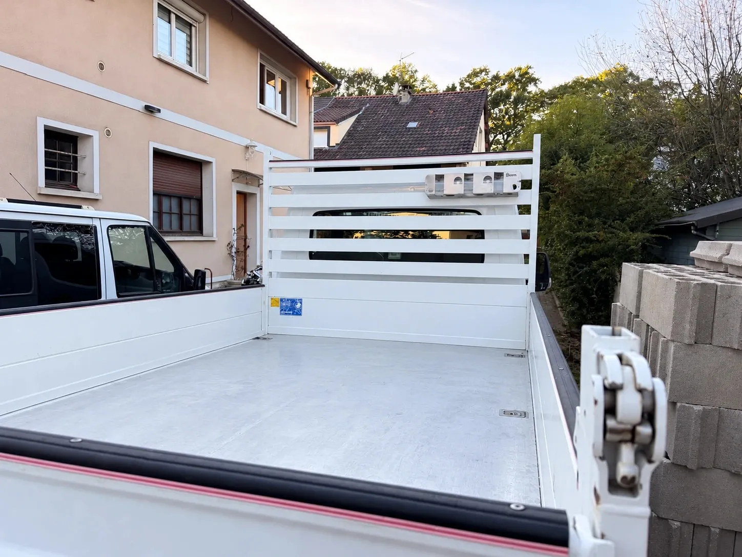 Benne vide d’un camion 3,5 t à ridelles garé devant une maison, à côté d’une pile de parpaings.