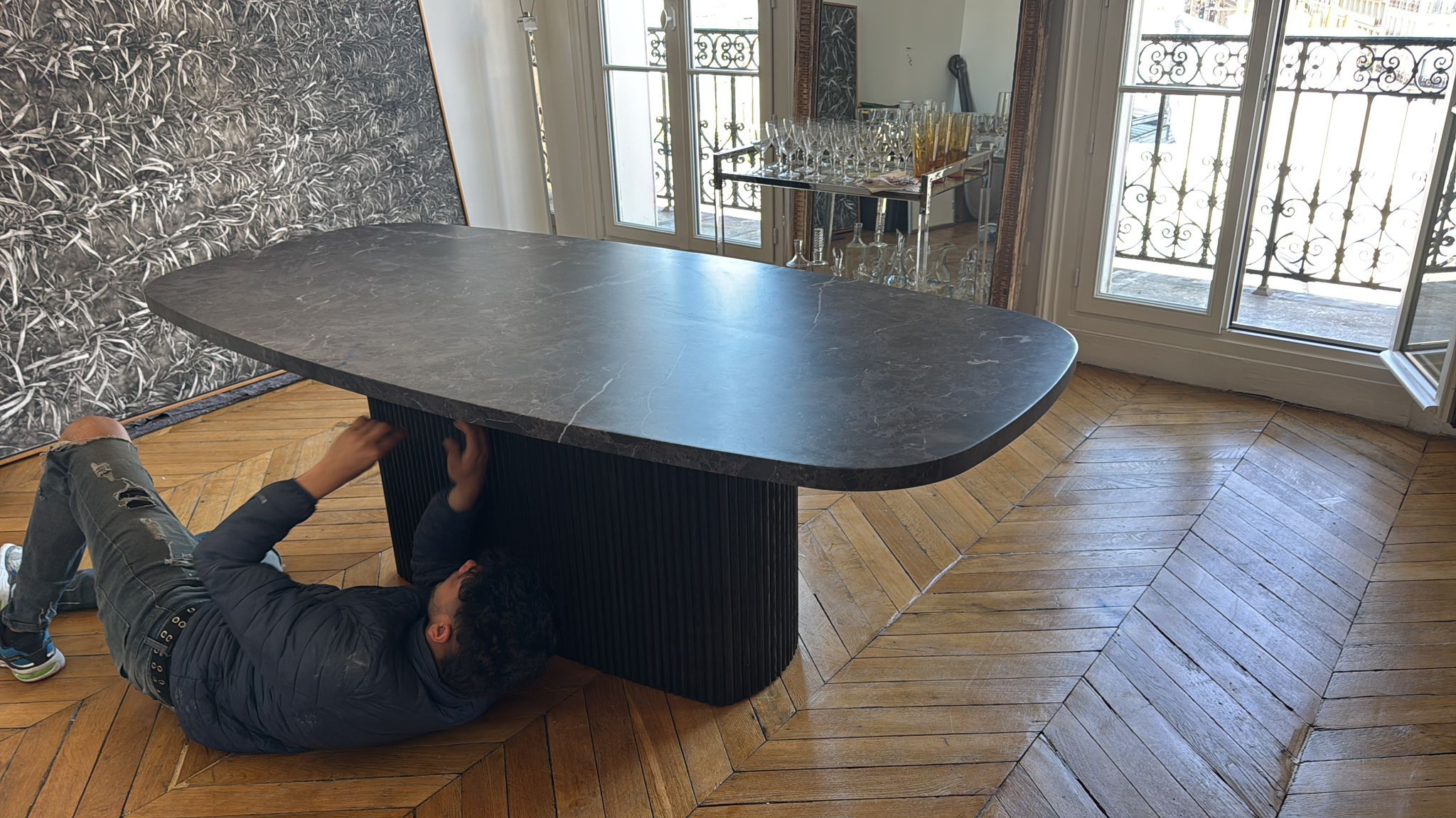 Un déménageur KAIROS fixe le piètement d’une table en pierre dans un appartement parisien au parquet en point de Hongrie.