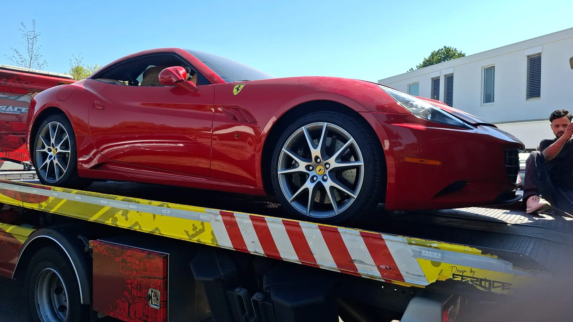 Une voiture de sport rouge sanglée sur le plateau d’un camion de transport, par temps ensoleillé.